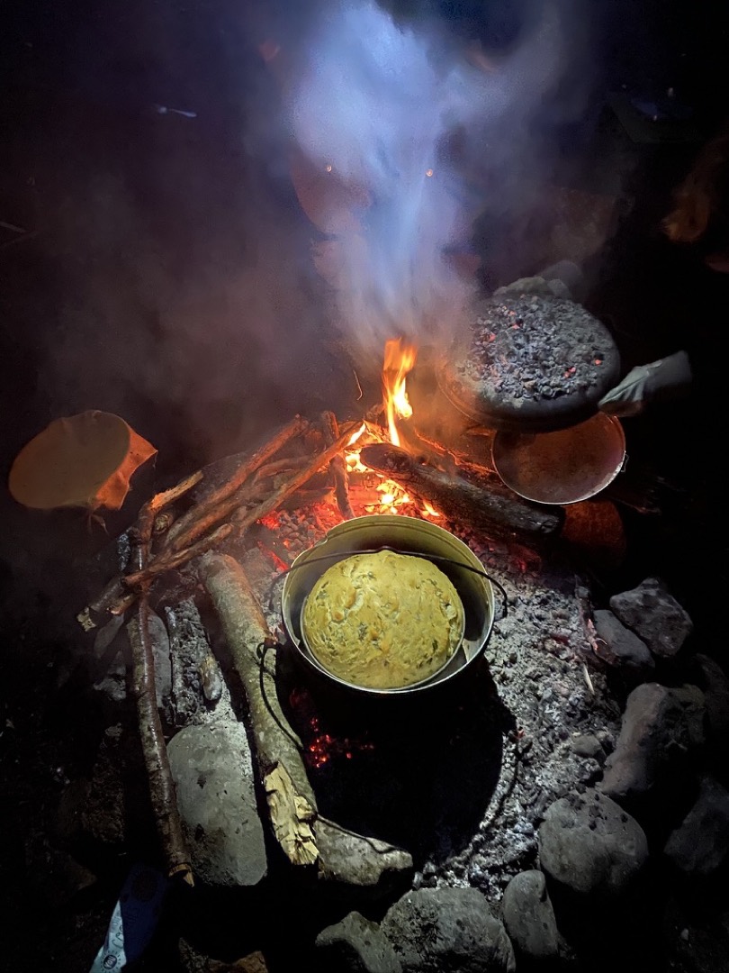 Brotteig im Metallkesser über Lagerfeuer bei Nacht